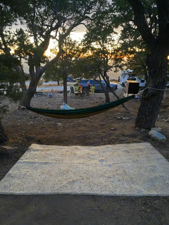 Serene RV rental campsite with a hammock, woven rug, people by a campfire, and a sunset glow through trees.. Keystone RV Bullet Crossfire 2021