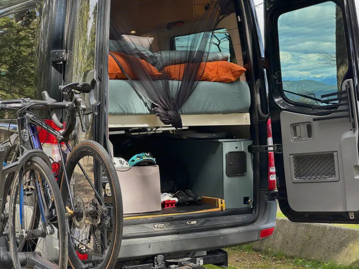 RV rental van's open rear reveals a bed with mosquito net, gear storage for helmets & shoes, plus bikes mounted outside for adventure.. Mercedes Sprinter 2007