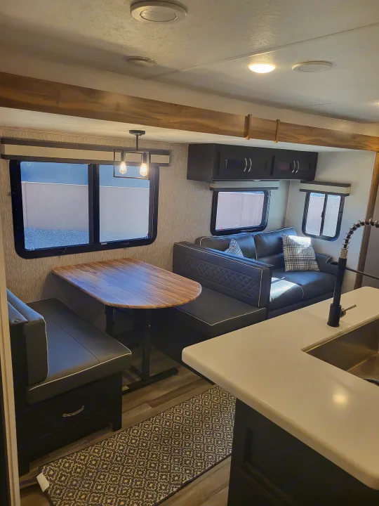 Modern RV rental interior: dining booth, cozy sofa, and kitchen with a sink. Stylish design for comfortable road trips.. Coachmen Freedom Express liberty edition 326bhdsle 2023