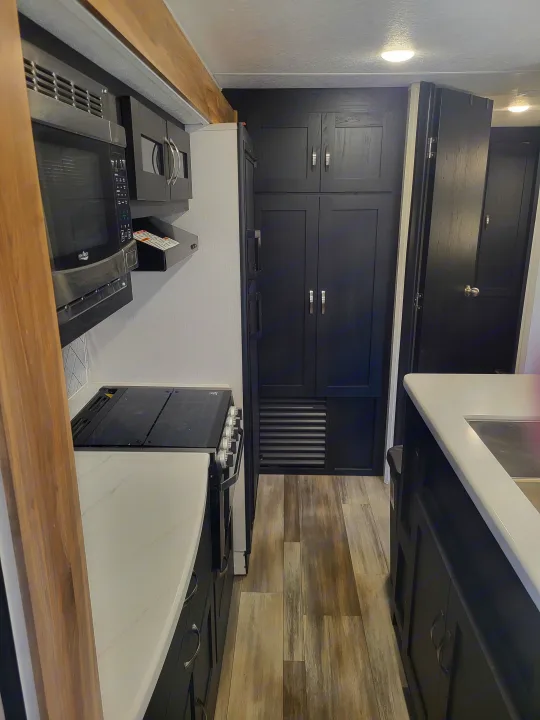 Spacious RV rental galley featuring black cabinets, white countertops, microwave, stove, and fridge. Ready for your travels!. Coachmen Freedom Express liberty edition 326bhdsle 2023