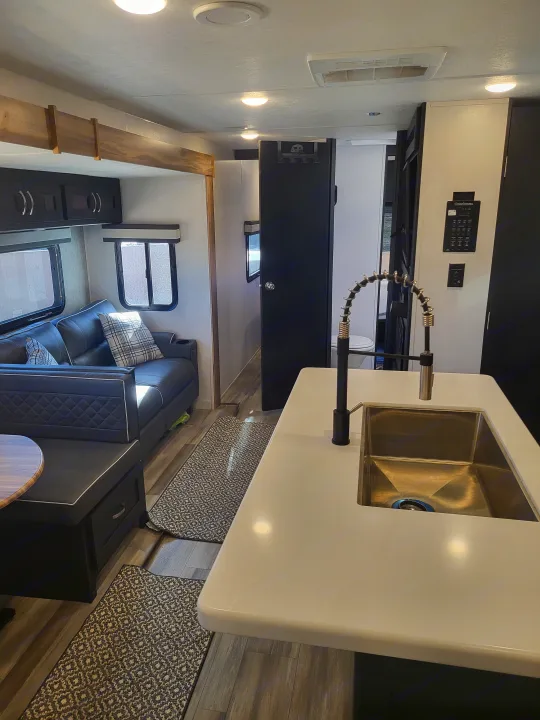 RV rental interior with a modern kitchen island, sink, and faucet, plus a comfortable sofa and dinette.. Coachmen Freedom Express liberty edition 326bhdsle 2023