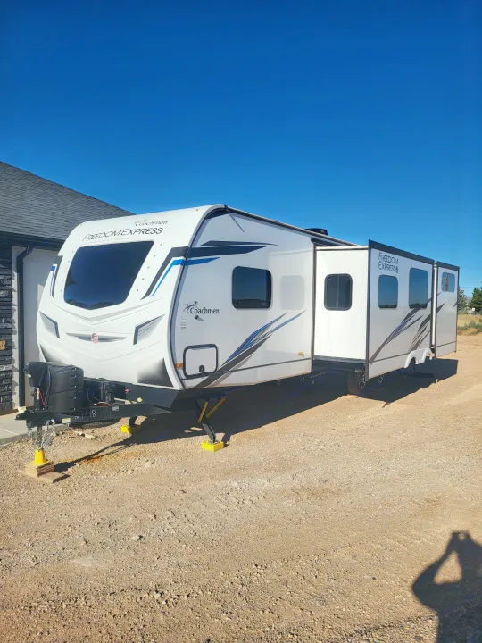 This white Coachmen Freedom Express rv rental, with slide-outs extended, is parked on gravel under a clear blue sky.. Coachmen Freedom Express liberty edition 326bhdsle 2023