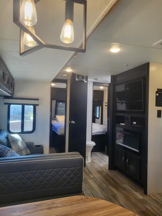 A bright rv rental interior showcases a living area, two sleeping zones, a bathroom, and an entertainment center with a fireplace.. Coachmen Freedom Express liberty edition 326bhdsle 2023
