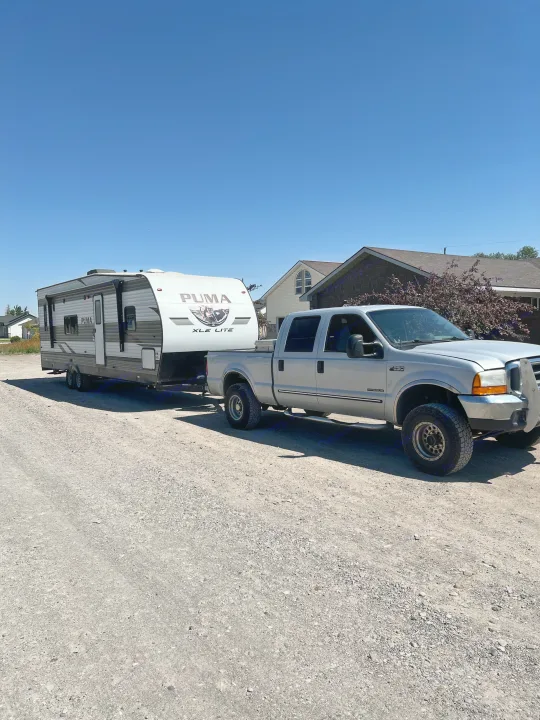 Silver F-250 truck towing a Puma XLE Lite RV on a gravel road. Ideal for an rv rental getaway or camping trip.. Palomino Puma 2021