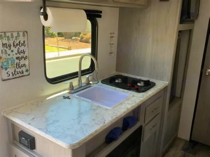Cozy RV rental kitchen: sink, two-burner stove, marble-look counter, and a fun '5-star' camping sign. Ready for adventures!. Coleman Lantern 2023