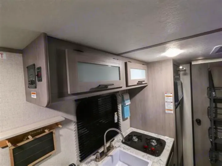 Interior of an RV rental kitchen: modern gray cabinets, sink, two-burner stovetop, and fridge for compact travel.. Coleman Lantern 2023
