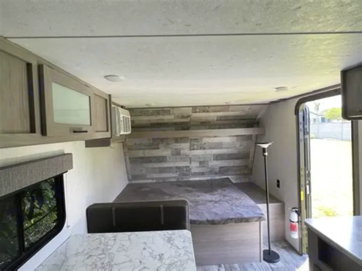 Explore this cozy RV rental interior: a bedroom with a unique wall, storage cabinets, a dinette, and an open door to the outside.. Coleman Lantern 2023
