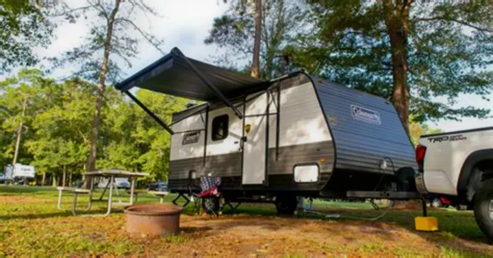 RV rental: A Coleman travel trailer is set up at a campsite, hitched to a white Toyota truck. A picnic table and fire pit are nearby.. Coleman Lantern 2023