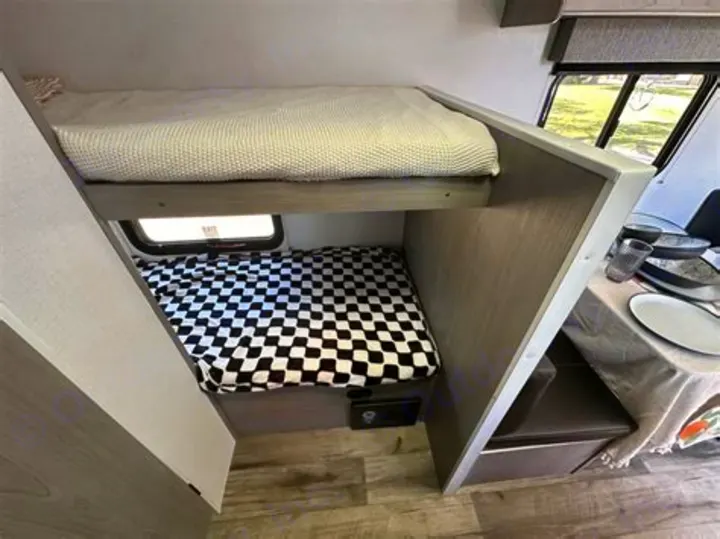 RV rental's cozy interior features bunk beds (top cream, bottom checkered), an exit window, and a dining table.. Coleman Lantern 2023
