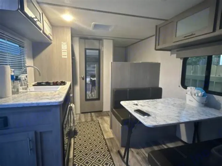 This clean RV rental interior features a kitchen, dinette with booth seating, and a full-length mirrored door, ready for travel.. Coleman Lantern 2023