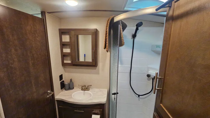 This RV rental bathroom features a vanity with sink, mirrored medicine cabinet, and a functional standing shower with curved door.. Crossroads RV Sunset Trail Super Lite 2018
