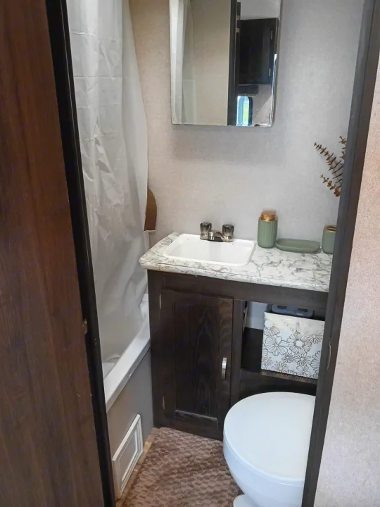 This compact RV rental bathroom features a small sink, toilet, shower, and mirror.. Keystone RV Springdale 2019