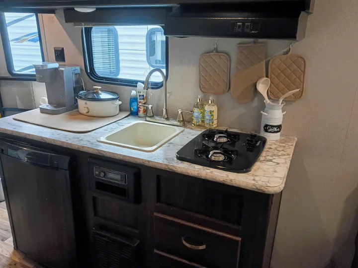 RV rental's compact kitchen features a coffee maker, sink, two-burner stove, mini-fridge, and cooking essentials.. Keystone RV Springdale 2019