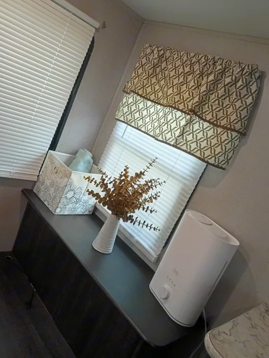 Cozy RV rental interior featuring white pleated blinds, a patterned valance, dried eucalyptus, and a humidifier on a dark shelf.. Keystone RV Springdale 2019