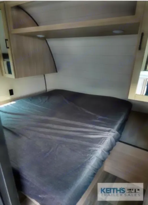 Cozy RV rental bedroom featuring a dark sheeted bed, overhead storage, and light wood-paneled interior for comfortable travel.. Highland Ridge RV Colt 2026