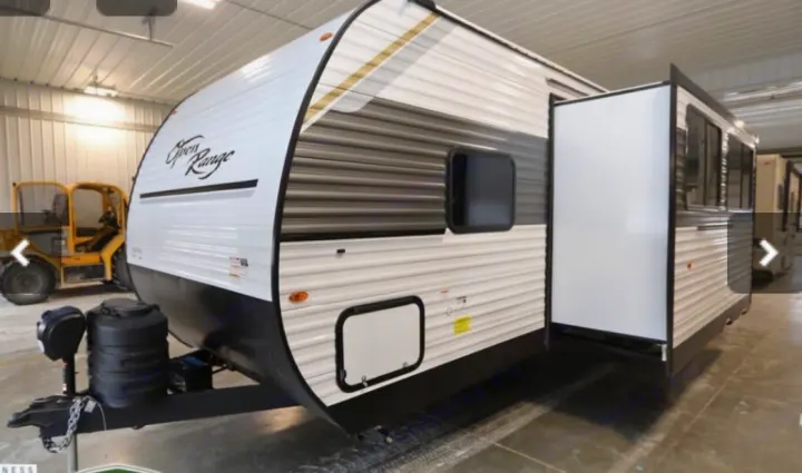 A white Open Range travel trailer with black and gold stripes, shown indoors with a side slide-out extended, perfect for RV rental.. Highland Ridge RV Colt 2026