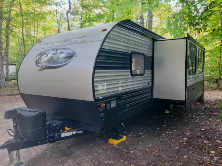 An RV rental, a gray Cherokee Limited travel trailer, is parked at a wooded campsite with its slide-out extended.. Forest River Cherokee 2021