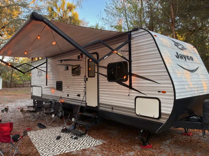 Relaxing RV rental setup: a travel trailer with illuminated awning, outdoor rug, camping chairs, and two dogs at a cozy campsite.. Jayco Jay Flight SLX 2017