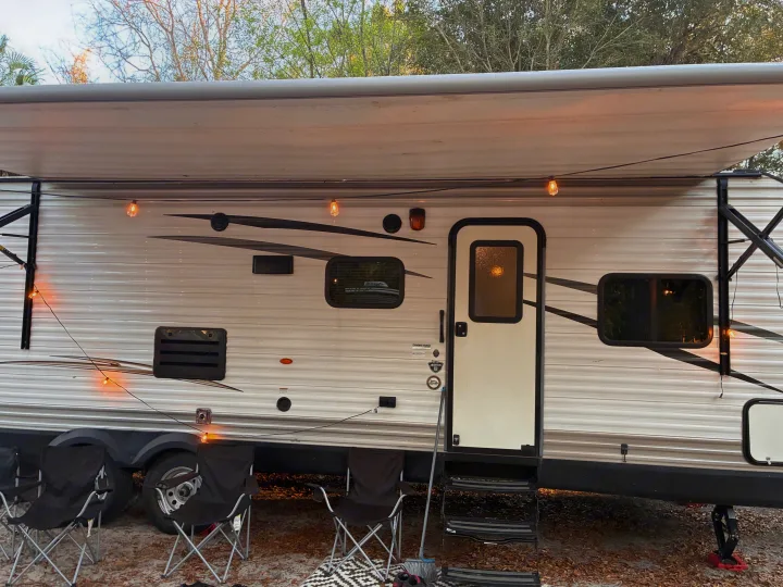 An RV rental at a campsite with its awning extended and warm string lights illuminating the side, offering a cozy outdoor space.. Jayco Jay Flight SLX 2017