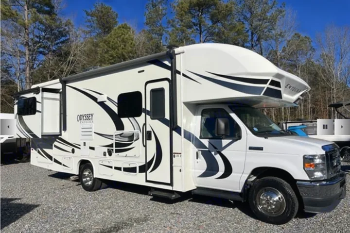 Explore with this white Entegra Odyssey Class C RV rental. Parked on gravel, it features a slide-out for extra space.. Entegra Coach Odyssey 2021