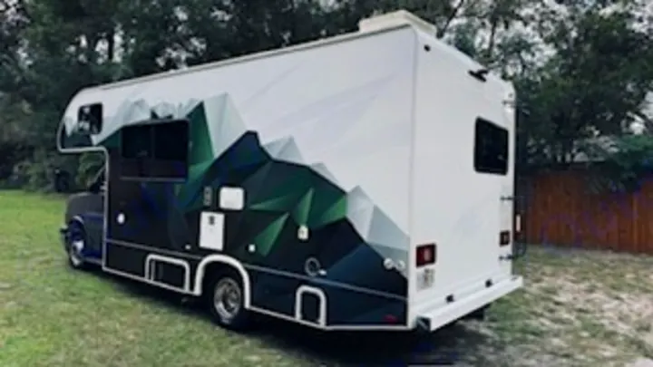 Stylish RV rental featuring green geometric mountain graphics, parked on grass. Ideal for your next travel adventure.. Thor Quantum LC 2022