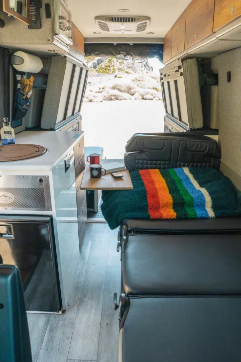 An RV rental camper van interior: kitchenette, seating with a rainbow blanket, and a beautiful outdoor view.. Storyteller Overland Storyteller Overland Class B 2022