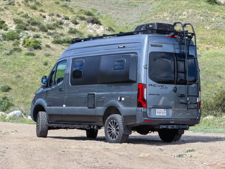 Rugged gray Winnebago Revel Sprinter adventure van, perfect for rv rental, parked on a dirt trail amidst green hills.. Winnebago Revel 2026