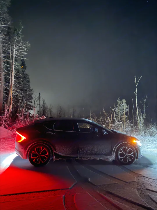 Modern car with glowing lights on snowy road at night among bare trees. Winter travel ready, explore **rv rental** options.. Kia EV6 Wind All Wheel Drive 2022