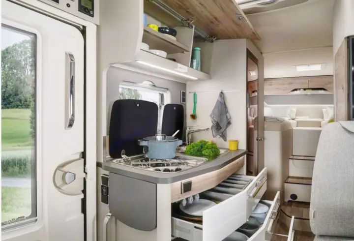Modern rv rental interior: A compact kitchen with stove, sink, and open drawers, leading to a cozy sleeping area in back.. HYMER EXISIS I 474 2025