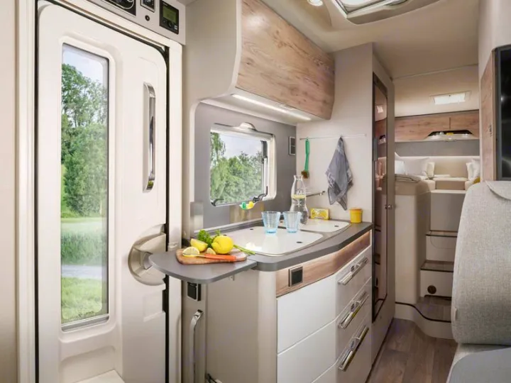 This modern rv rental features a compact kitchen with a sink, a cozy rear bedroom, and a door looking out to nature.. HYMER EXISIS I 474 2025