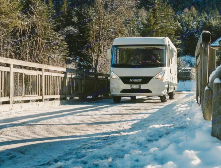 White Hymer RV rental on a snowy bridge in a winter mountain forest. Perfect for winter travel adventures.. HYMER EXISIS I 474 2025