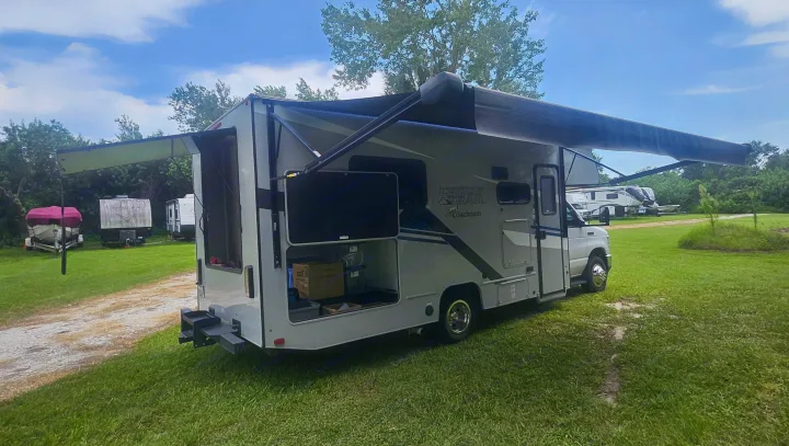 RV rental: A Coachmen Cross Trail motorhome with extended awnings and an outdoor TV, parked at a grassy campsite.. Coachmen Cross Trail 2023