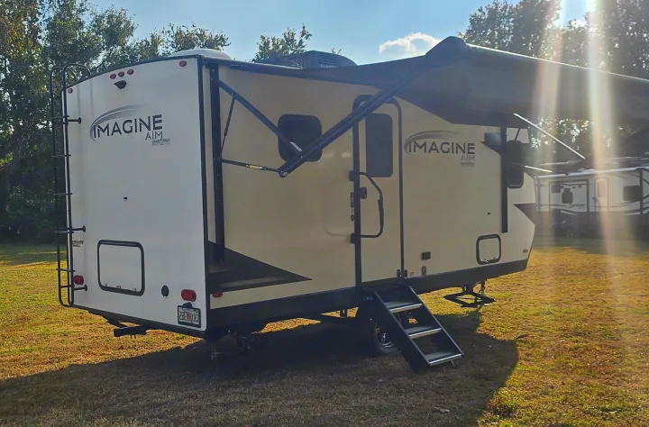 An Imagine Aim Grand Design RV rental, a travel trailer, is parked on grass with its awning extended.. Grand Design Imagine AIM 2023
