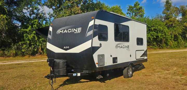 RV rental: A white and black Imagine Aim travel trailer ready for camping adventures in a natural, grassy setting with trees.. Grand Design Imagine AIM 2023