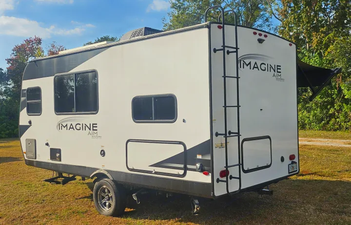 White Imagine AIM travel trailer rv rental with an awning, parked on grass outdoors, ready for your next adventure.. Grand Design Imagine AIM 2023