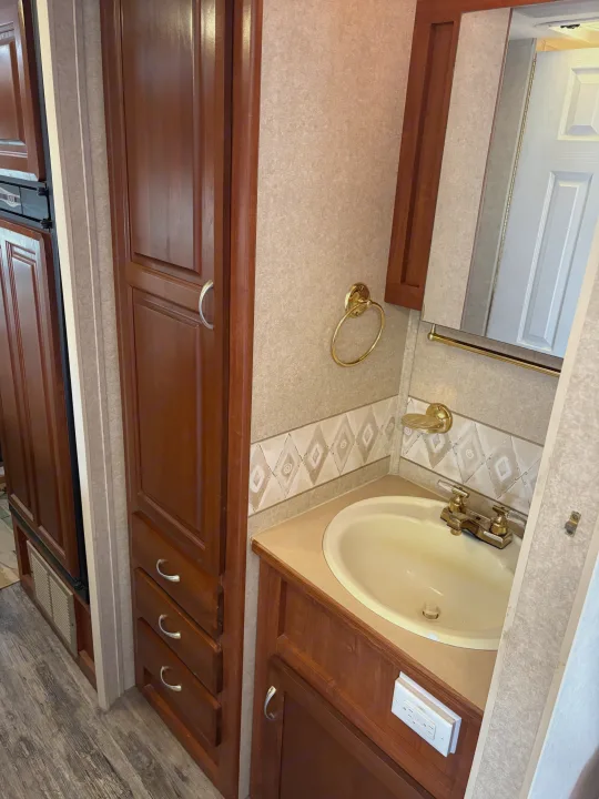 A cozy RV rental bathroom featuring a sink, mirror, golden fixtures, and ample wood-paneled storage.. Jayco Granite Ridge 2004