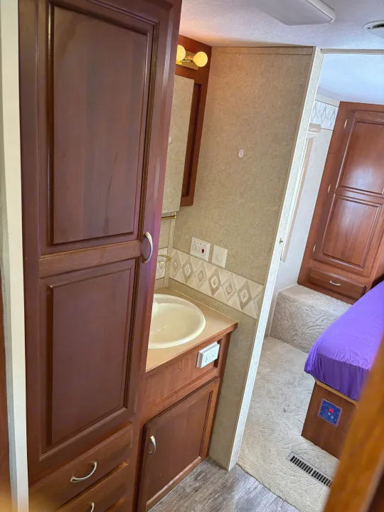 RV rental interior showing a small bathroom sink/vanity area and a carpeted bedroom with a purple bed.. Jayco Granite Ridge 2004