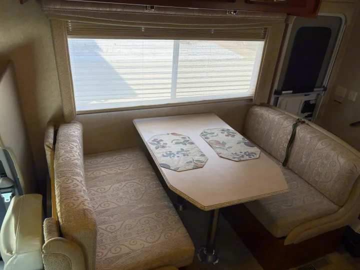 Cozy RV rental dinette featuring comfortable bench seating, a tabletop with placemats, and a window with blinds.. Jayco Granite Ridge 2004