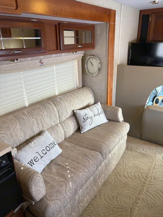 Cozy RV rental interior shows a patterned couch with "welcome" & "stay awhile" pillows, wood cabinets, and blinds.. Jayco Granite Ridge 2004