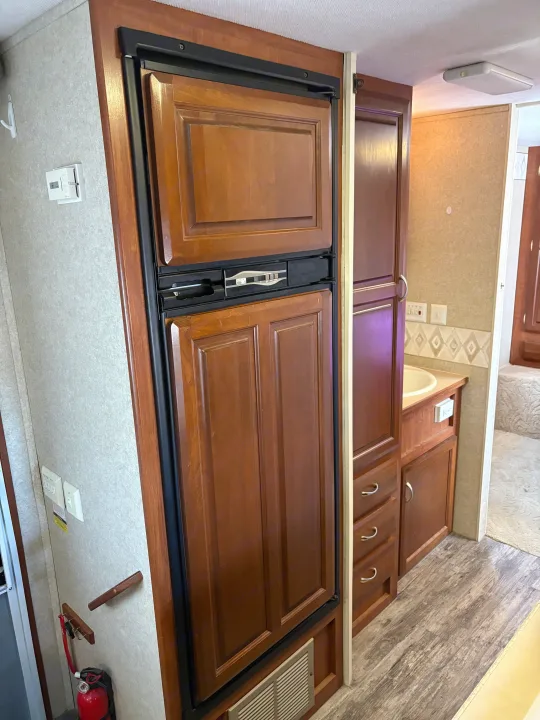 RV rental interior with a wood-paneled refrigerator, bathroom vanity, and wall-mounted controls.. Jayco Granite Ridge 2004