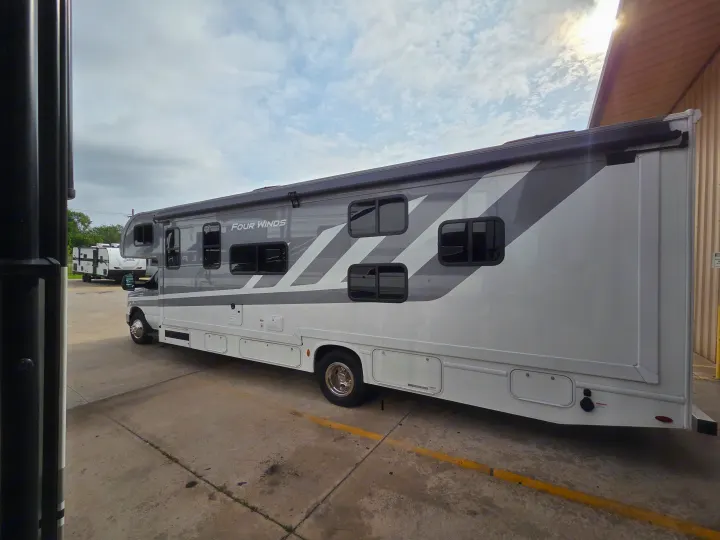 A large grey and white Four Winds motorhome with an awning, parked in a lot, ready for your rv rental adventure.. Four Winds 31E 2026