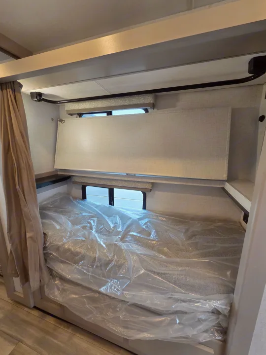 RV rental bunk bed interior, showing a lower mattress with protective plastic and an upper fold-down bunk/safety barrier.. Four Winds 31E 2026