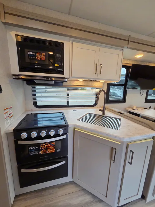 A bright and compact RV rental kitchen featuring a Contoure microwave, stove, and sink, alongside light cabinetry and countertops.. Four Winds 31E 2026