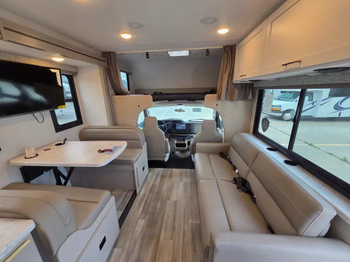 RV rental interior showcasing a modern living space with a dinette, sofa with seatbelts, and the driver's cabin upfront.. Four Winds 31E 2026