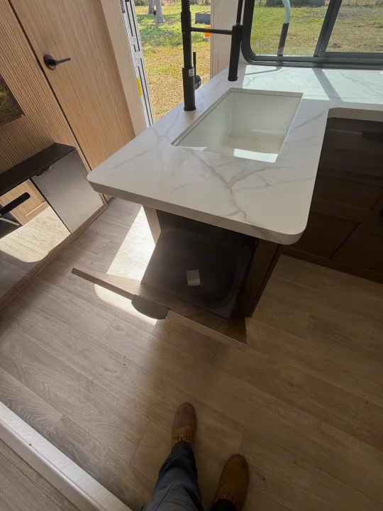 RV rental kitchen with a white marble-look counter, black faucet, and open drawer revealing storage. Sunlight streams across the modern interior.. Forest River Salem Cruise-Lite 2026