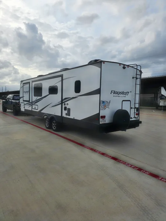 A white Flagstaff Super Lite travel trailer RV rental hitched to a black pickup truck, parked on a concrete lot.. Forest River Flagstaff Super Lite 2022