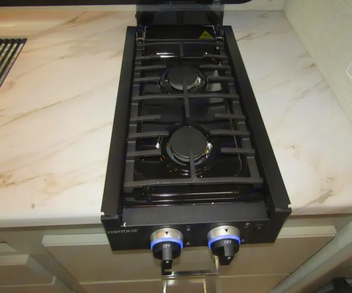 This RV rental features a modern Contoure two-burner gas cooktop with illuminated controls, set in a marble-look countertop.. Thor Chateau 2025