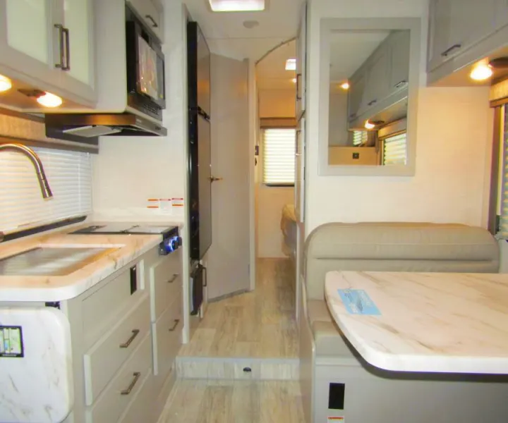 Modern RV rental interior featuring a light-toned kitchen with a sink, stove, microwave, and an adjacent dining booth.. Thor Chateau 2025