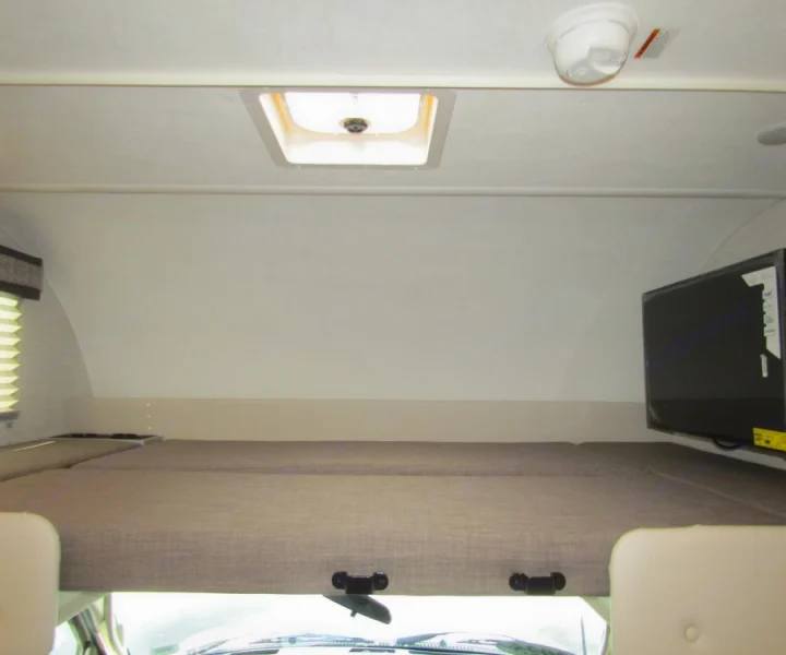 Overhead bunk bed with a ceiling vent, mounted TV, and front view of an RV rental, offering comfortable sleeping quarters.. Thor Chateau 2025
