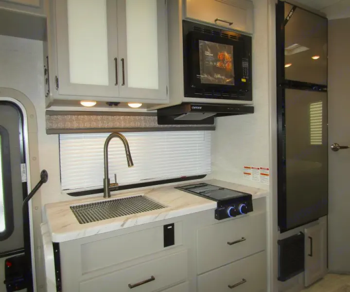 Modern RV rental kitchen with a sink, microwave, fridge, stovetop, and light gray cabinets. Compact & well-equipped.. Thor Chateau 2025